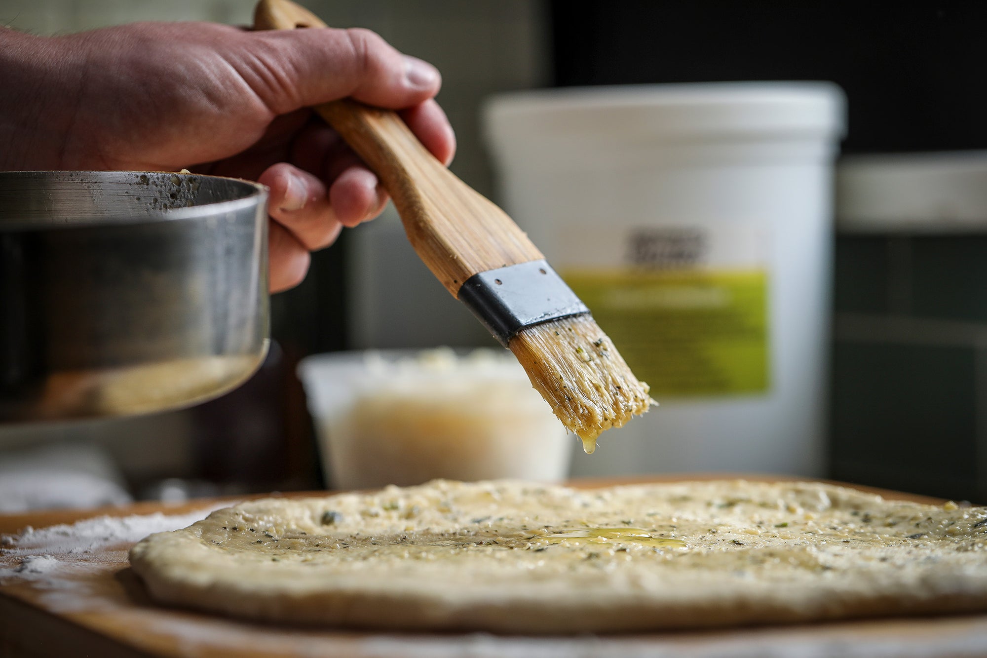 Spreading melted Epicurean Butter on pizza from 5 lb foodservice tub